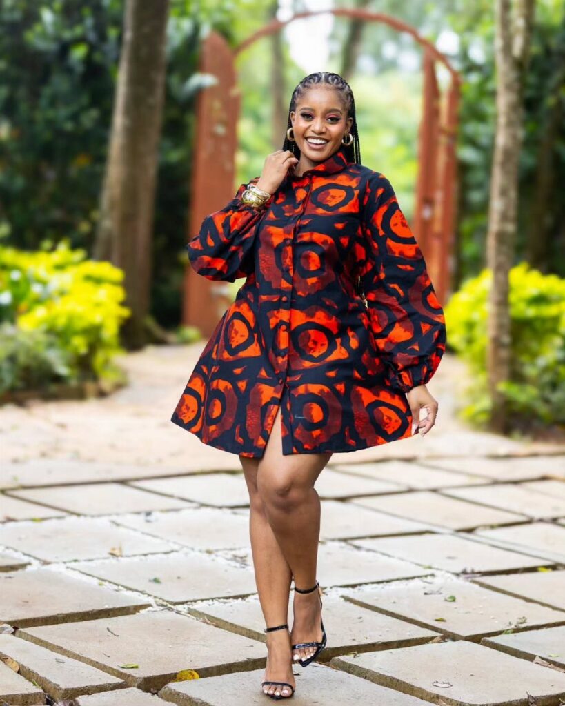 A woman smiling in a short orange and black patterned dress standing on a stone path.