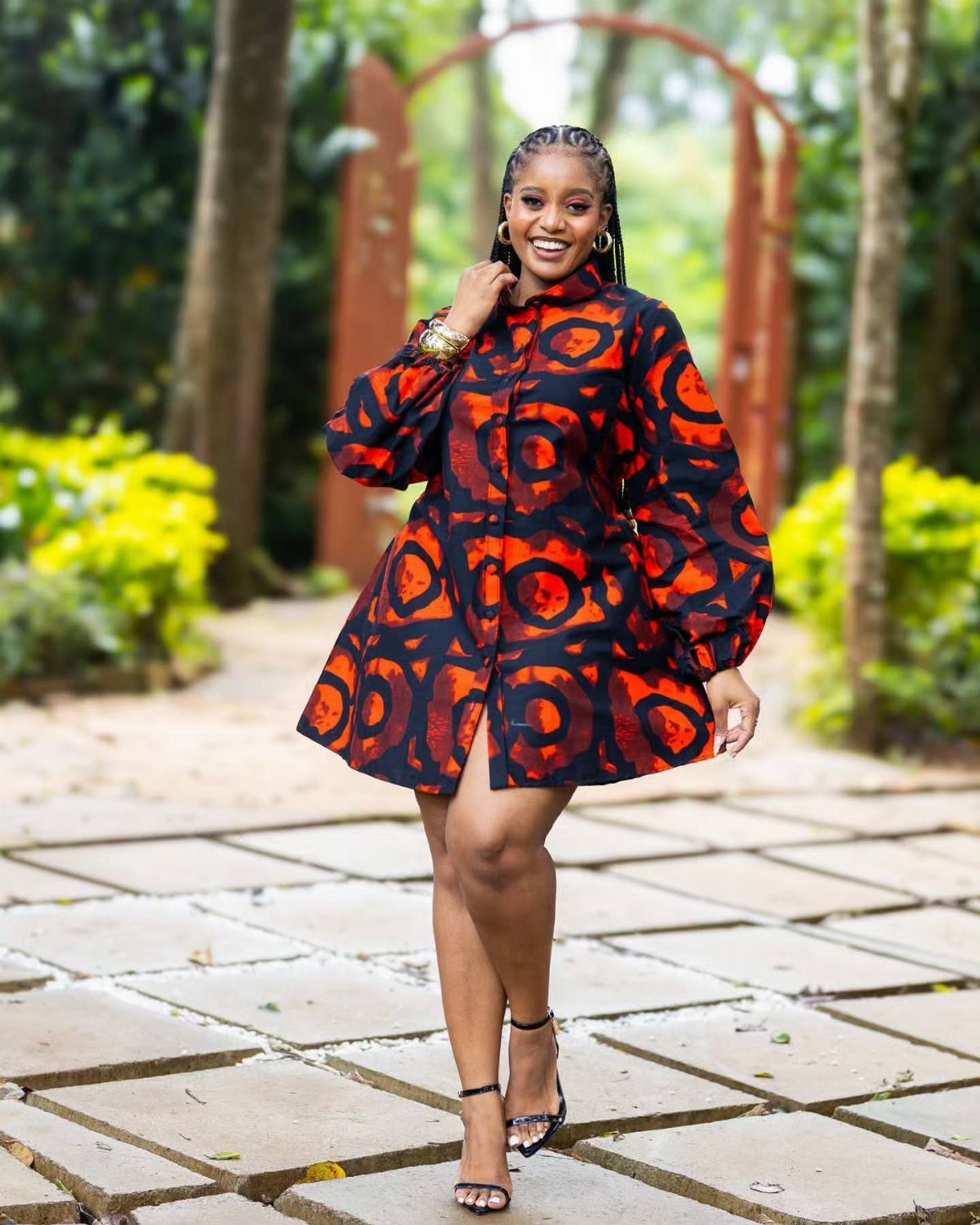 A woman smiling in a short orange and black patterned dress standing on a stone path.