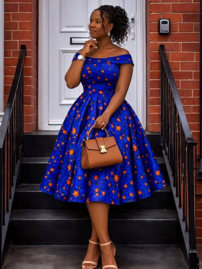 A woman posing in a blue and orange patterned structured midi dress holding a brown handbag.