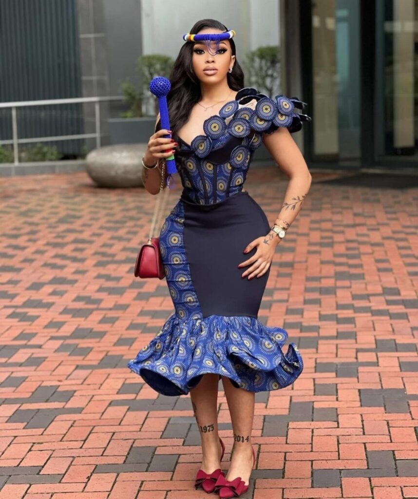 A woman in a blue patterned mermaid-style dress posing on a brick walkway outdoors.