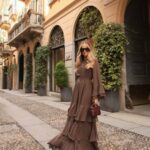 Woman in a tiered brown maxi dress and sunglasses standing on a cobblestone street.