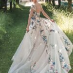 Woman in a floral embroidered empire-waist gown standing in a sunlit garden.