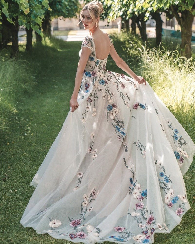 Woman in a floral embroidered empire-waist gown standing in a sunlit garden.