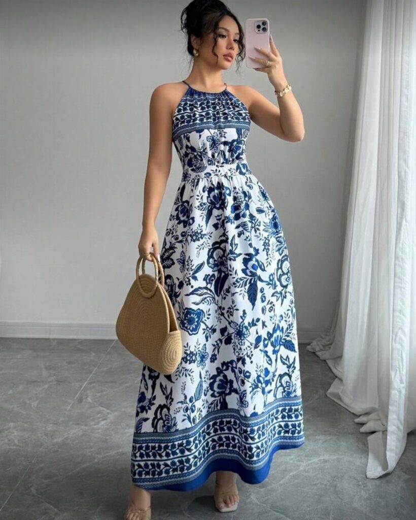 A woman in a blue and white floral maxi dress holding a straw handbag.