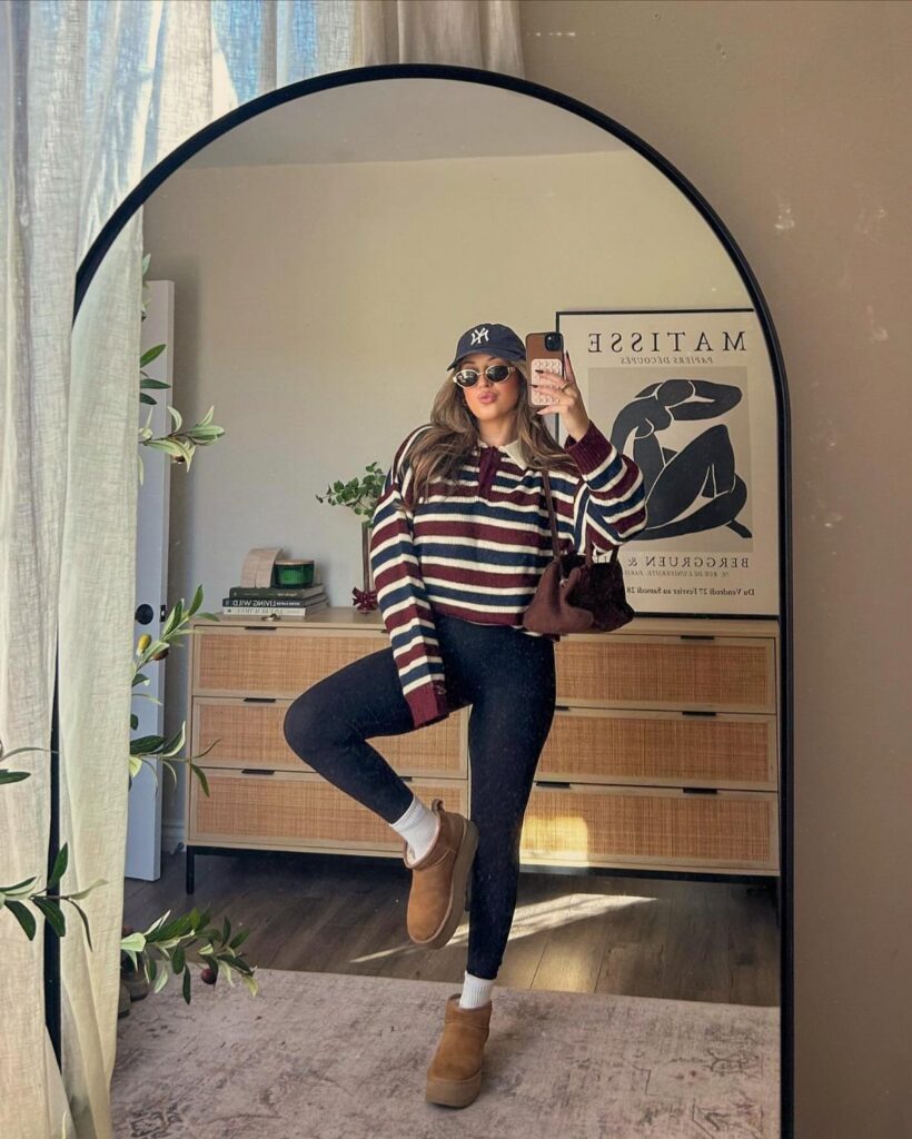 A woman posing in a mirror wearing a striped sweater, black leggings, and tan boots.