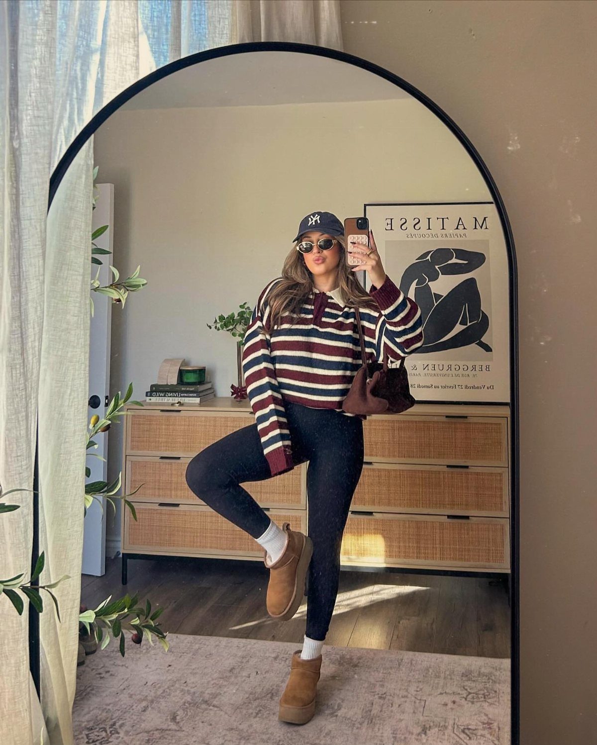 A woman posing in a mirror wearing a striped sweater, black leggings, and tan boots.
