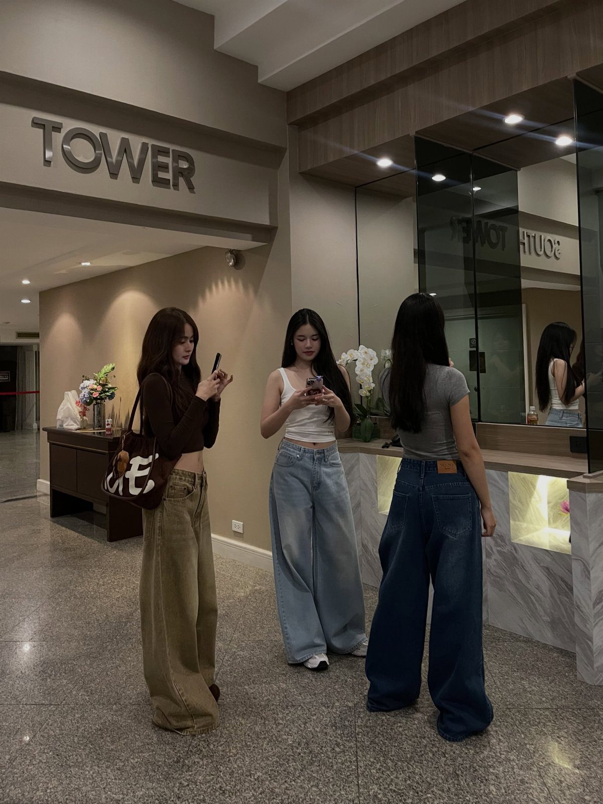 Three women standing indoors wearing various styles of wide-leg denim and casual trousers.