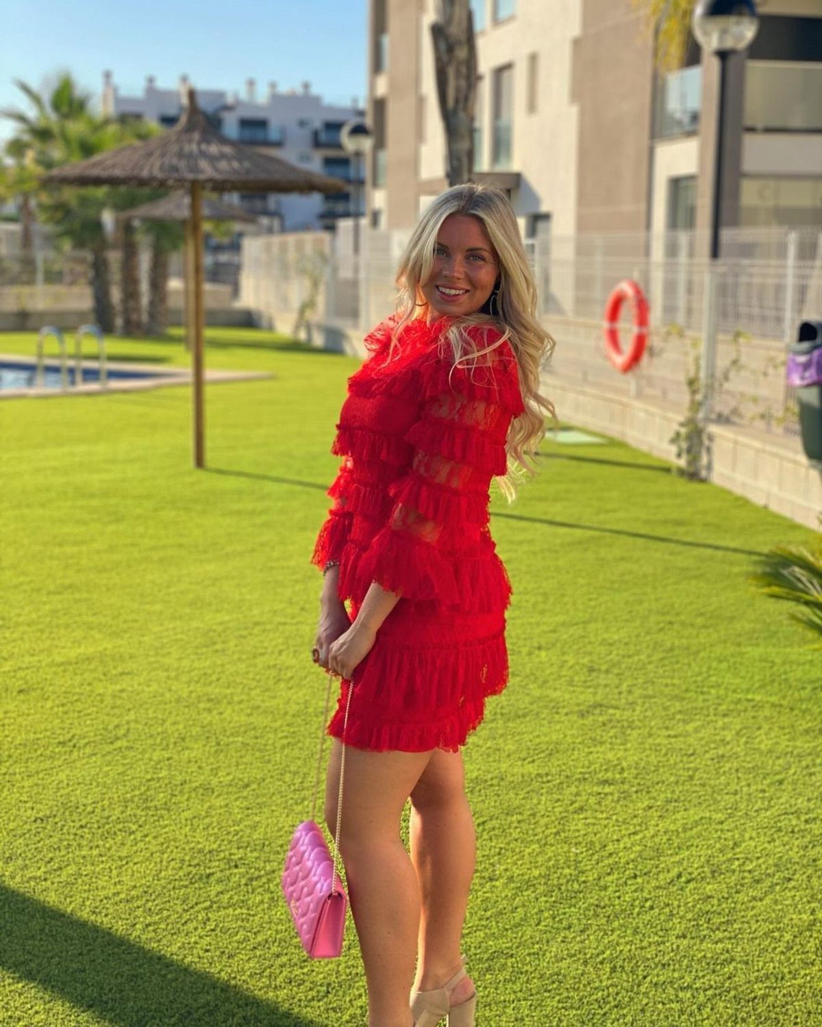 A smiling woman posing in a bright red tiered ruffled dress on a green lawn.