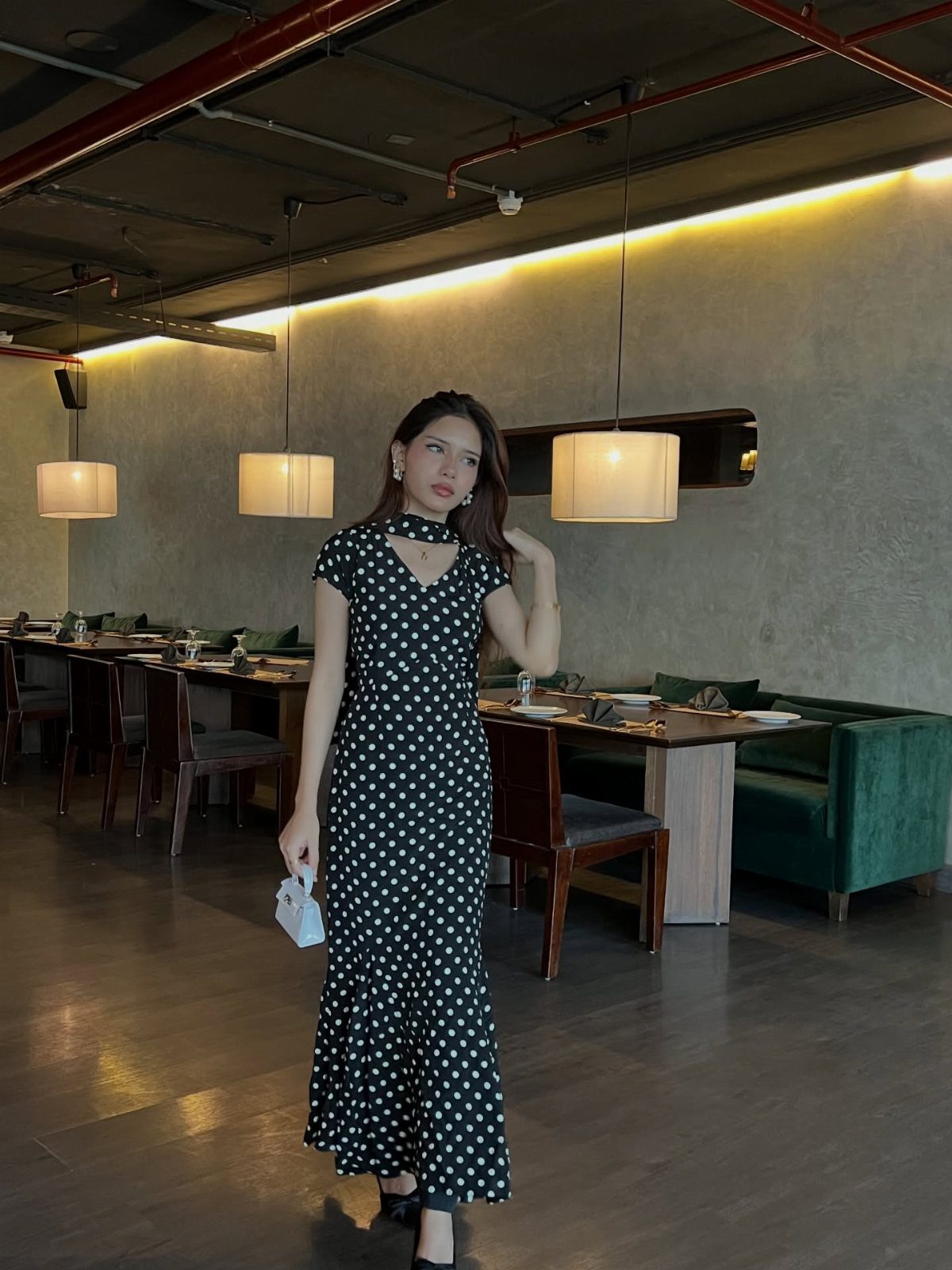 A woman posing in a black and white polka dot midi dress inside a restaurant.