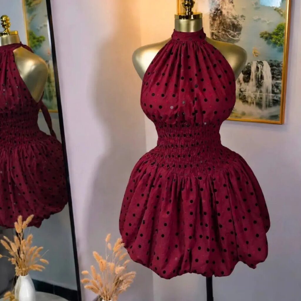 A maroon polka-dot halter neckline dress displayed on a gold mannequin stand.