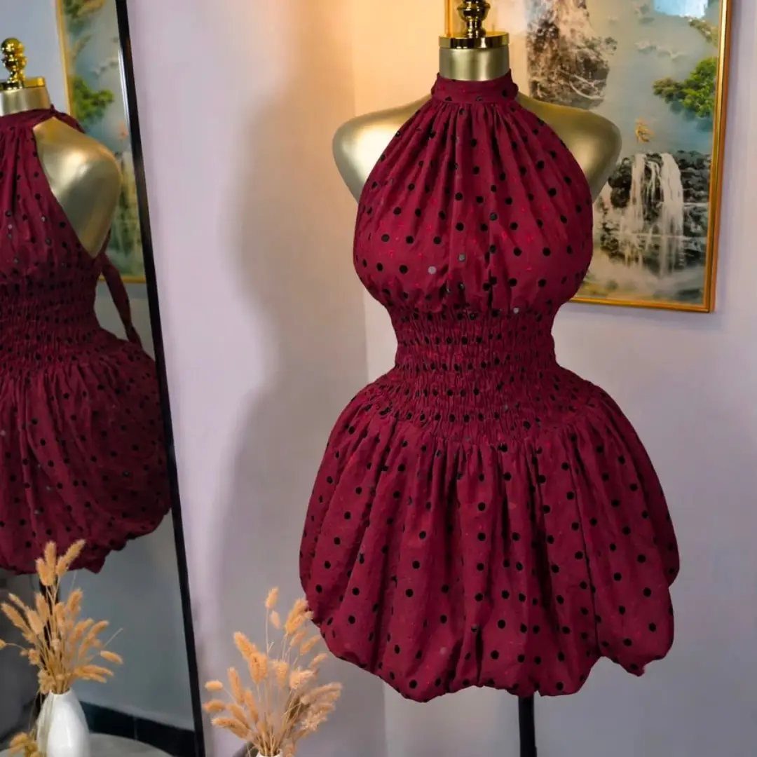 A maroon polka-dot halter neckline dress displayed on a gold mannequin stand.