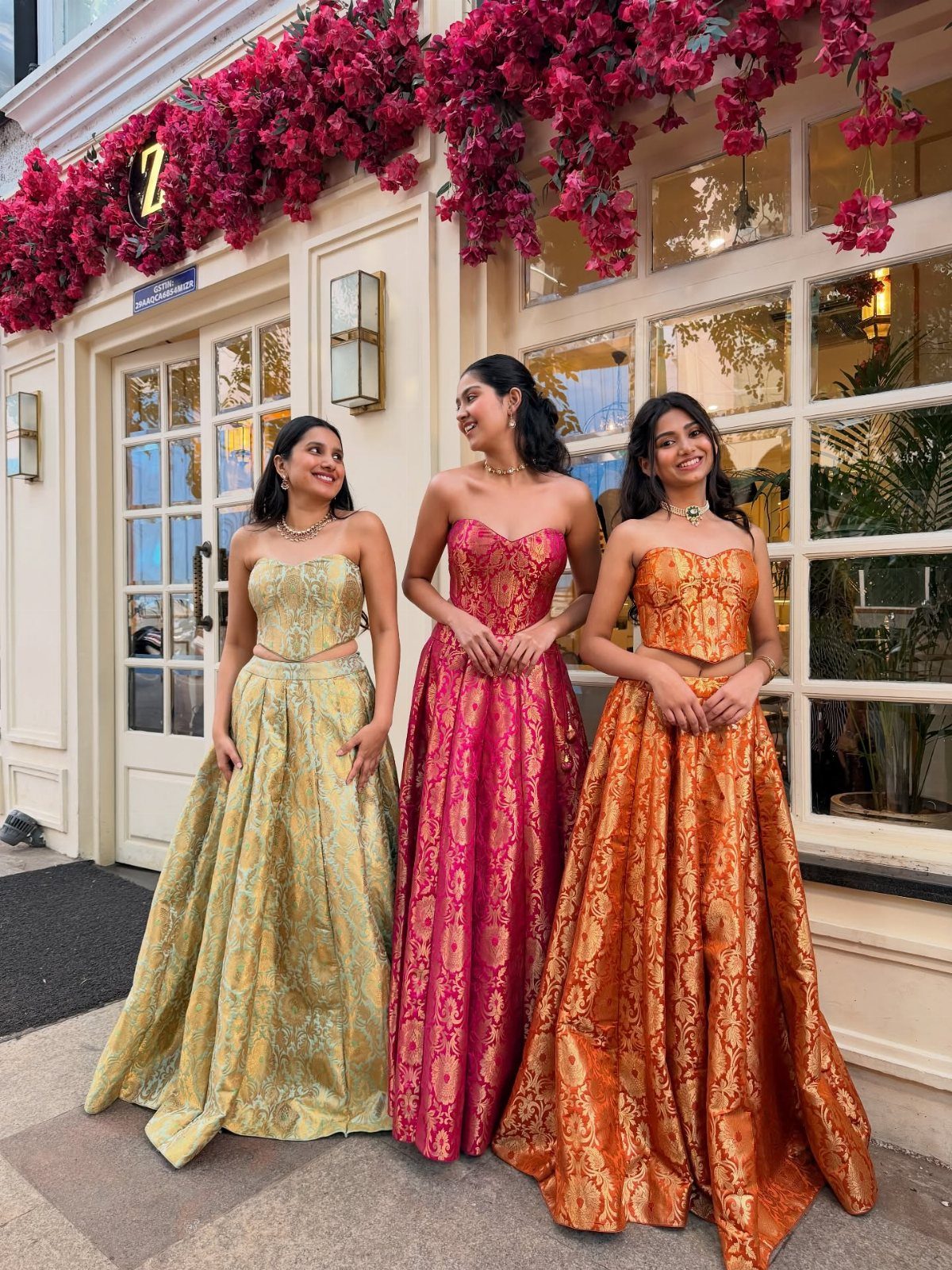 Three women posing in colorful, modern Indian-style patterned lehenga skirts and strapless tops.