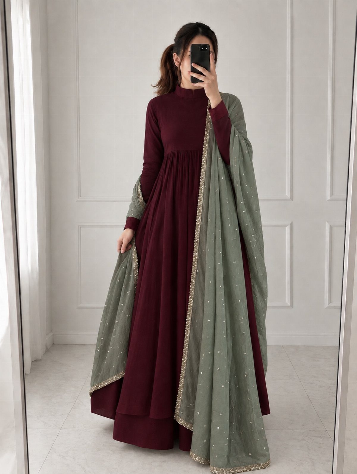 Woman in a maroon maxi dress and sage green embroidered dupatta taking a mirror selfie.