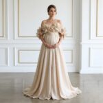 Pregnant woman wearing a champagne floral maternity gown standing in a white paneled room.
