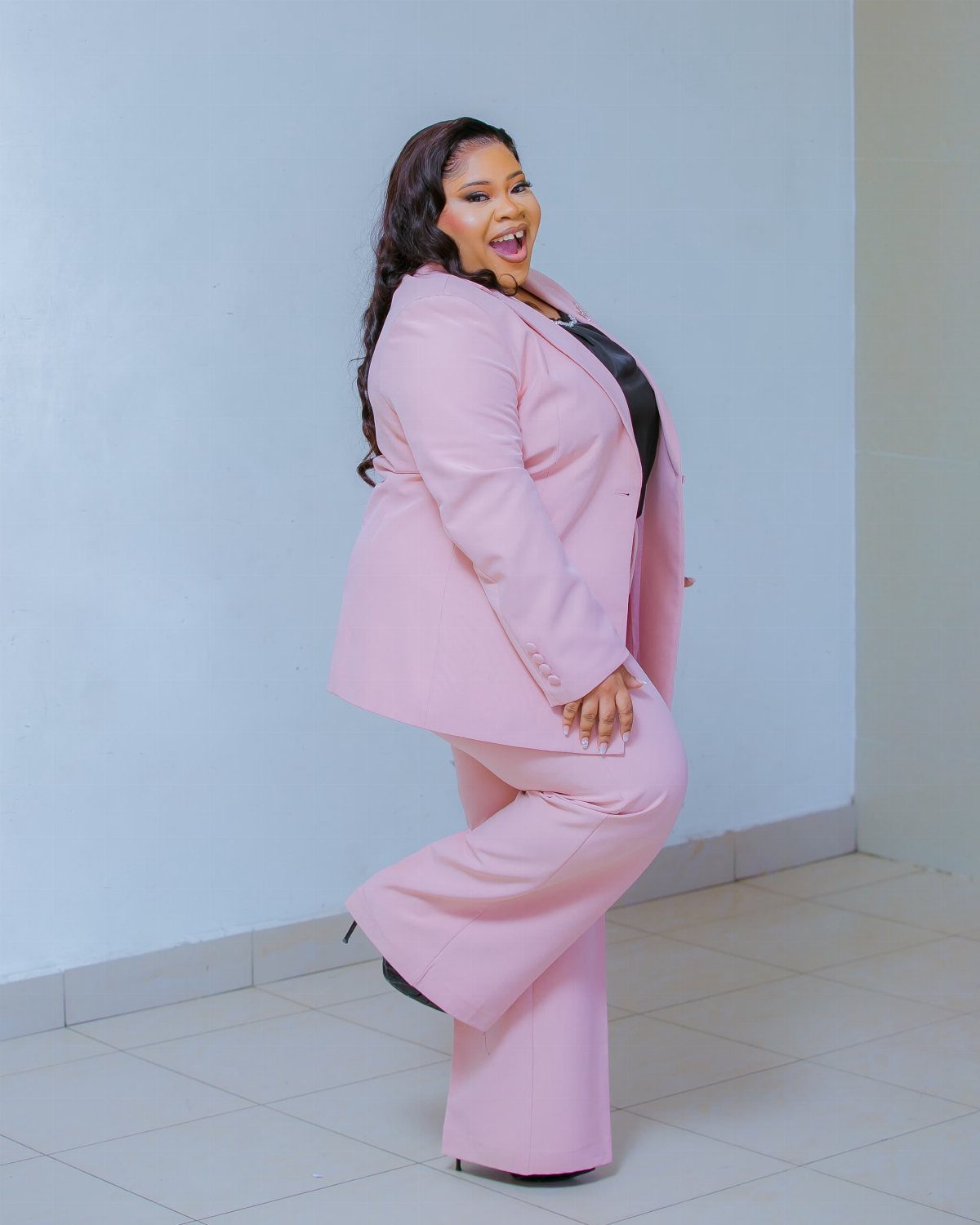 A smiling woman posing in a light pink blazer and matching wide-leg trousers.