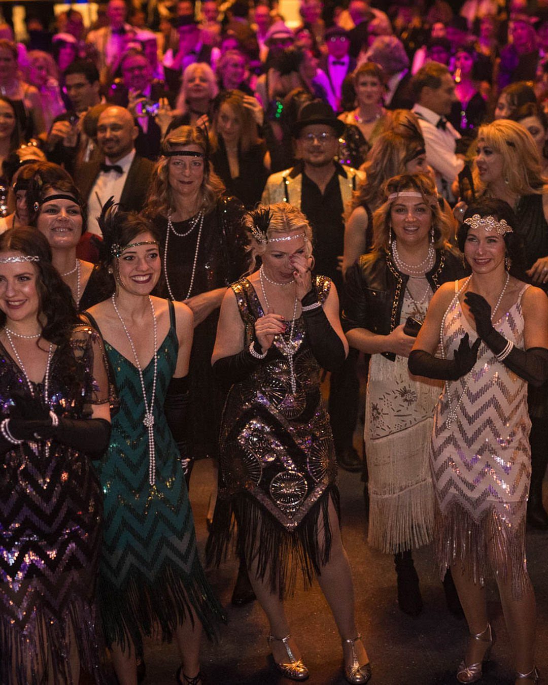 Women wearing sequined flapper dresses and pearl necklaces posing at a themed party.