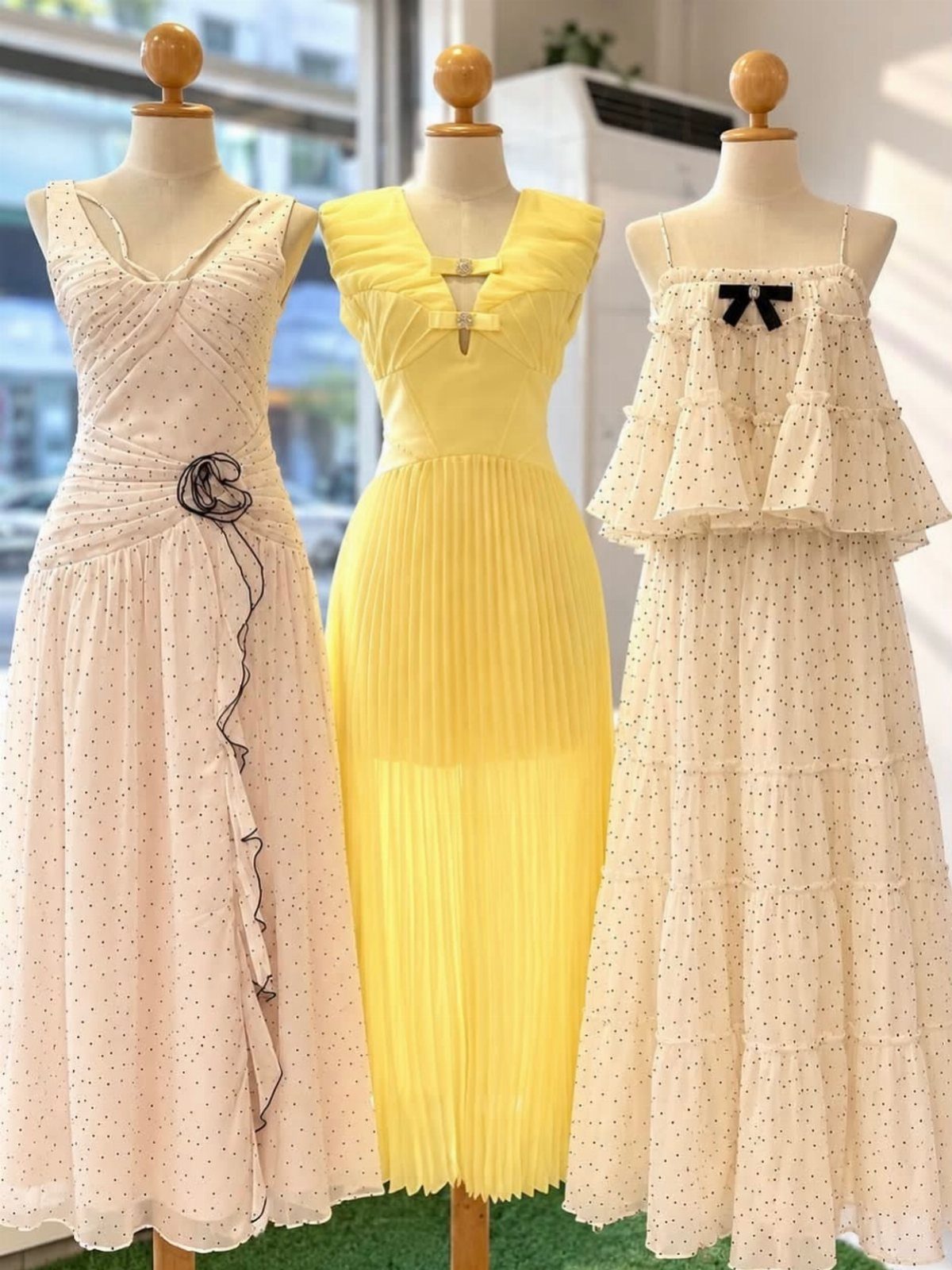 Three different summer dresses displayed on mannequins in a bright room.