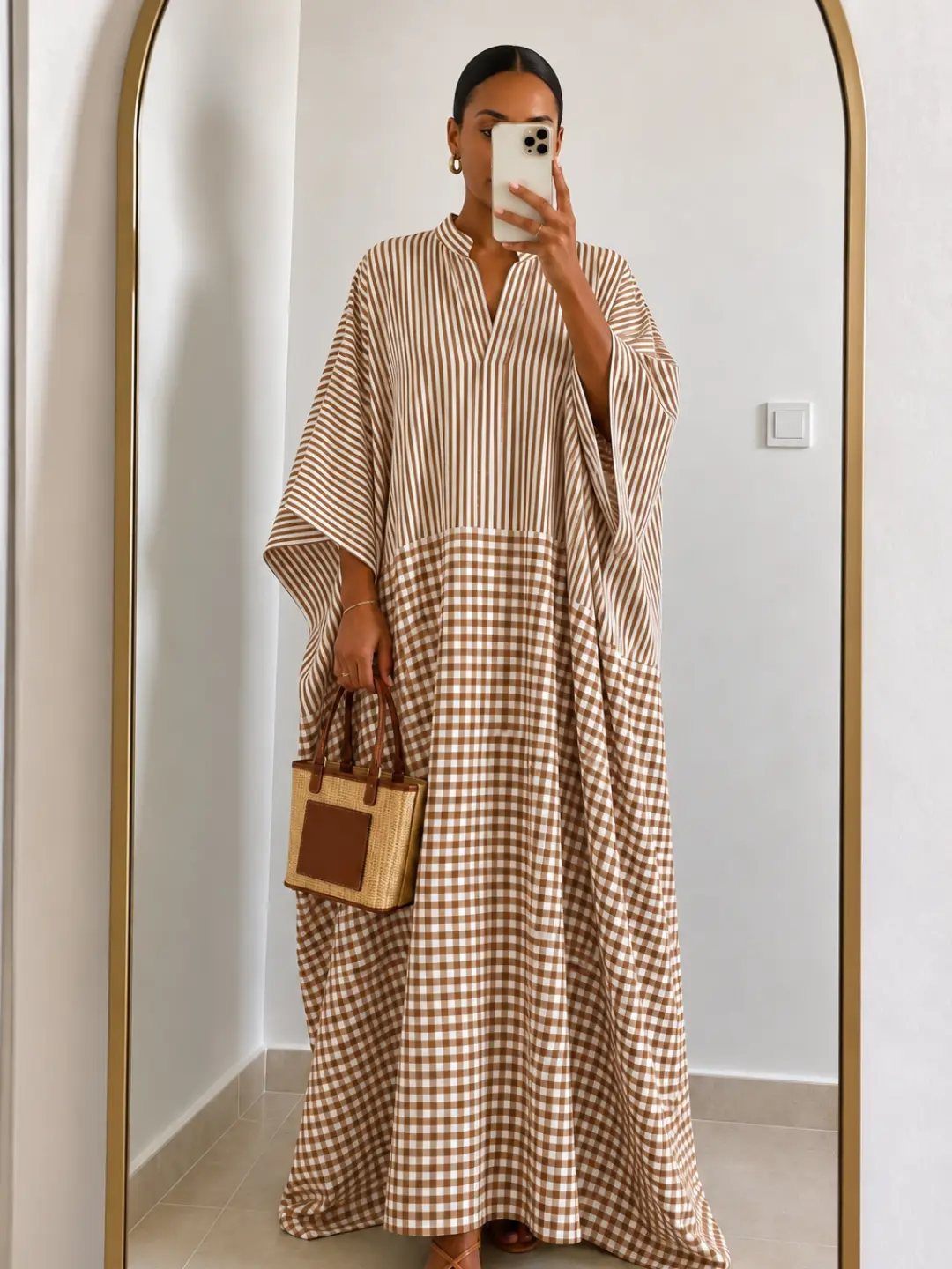Woman in a long, striped and gingham patterned kaftan dress taking a mirror selfie.