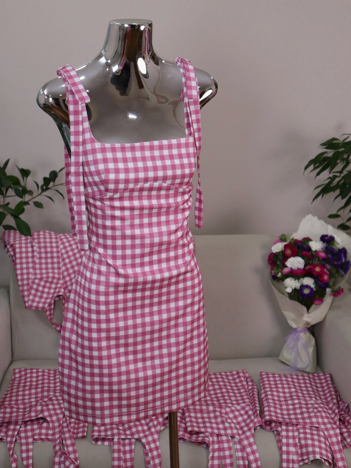 Pink and white gingham mini dress displayed on a silver mannequin against a white sofa.