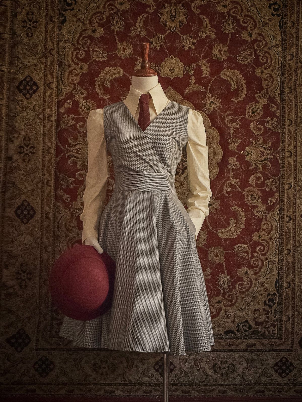 A grey patterned wrap dress on a mannequin worn over a cream blouse and red tie.