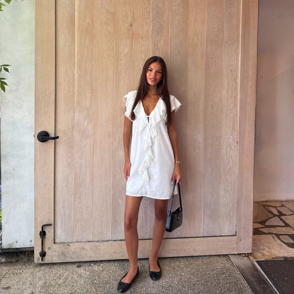 A woman in a white ruffled dress posing in front of a large wooden door.
