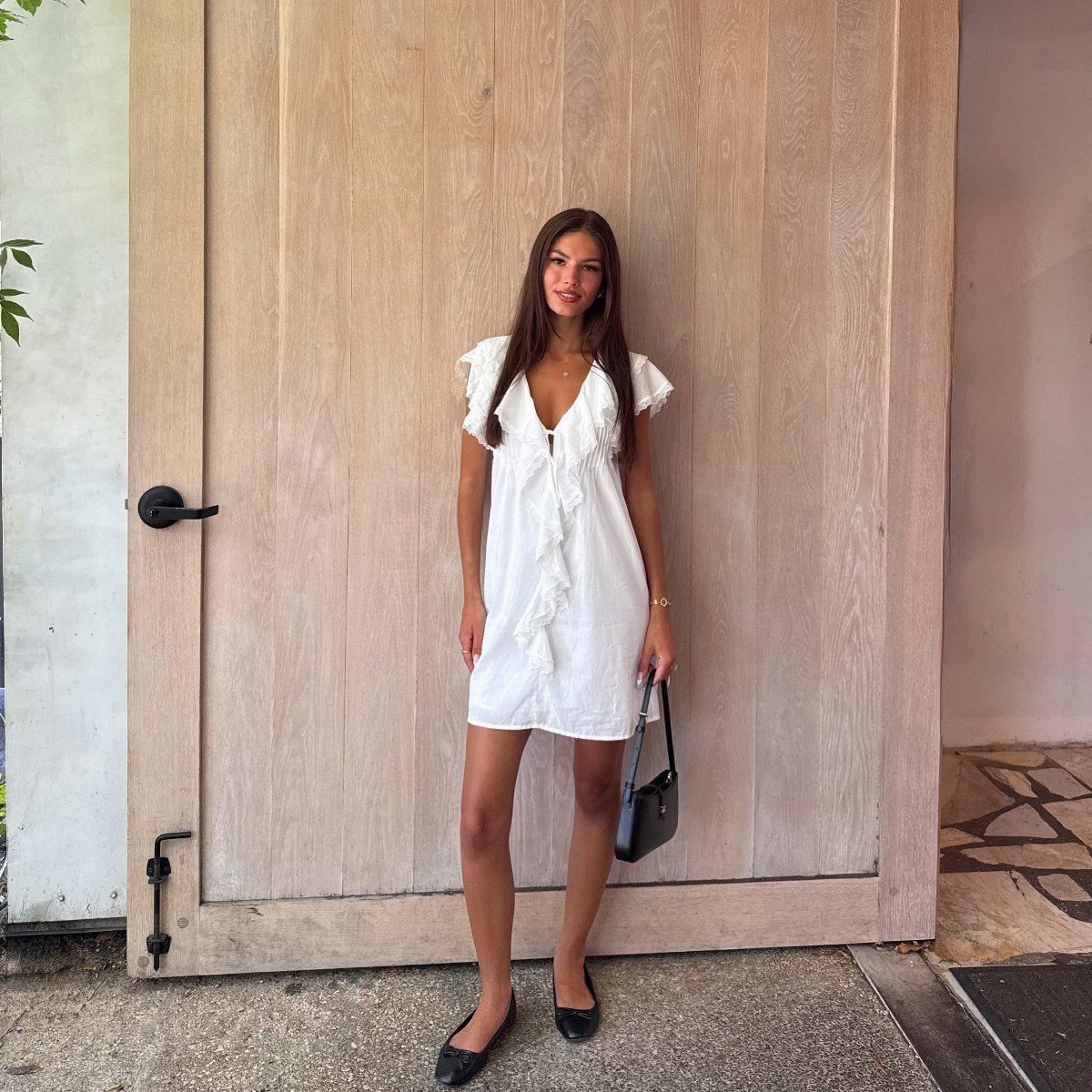 A woman in a white ruffled dress posing in front of a large wooden door.