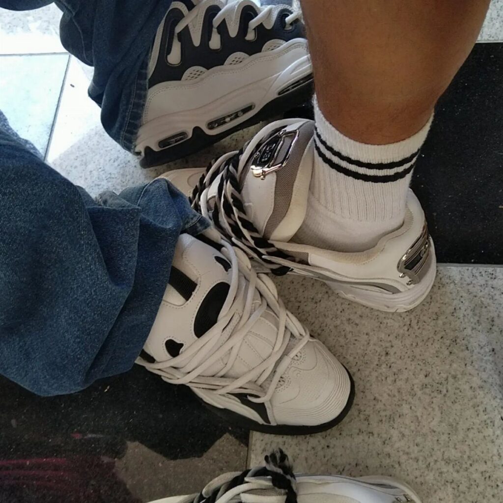 Several pairs of chunky white and black sneakers worn with denim jeans and white socks.
